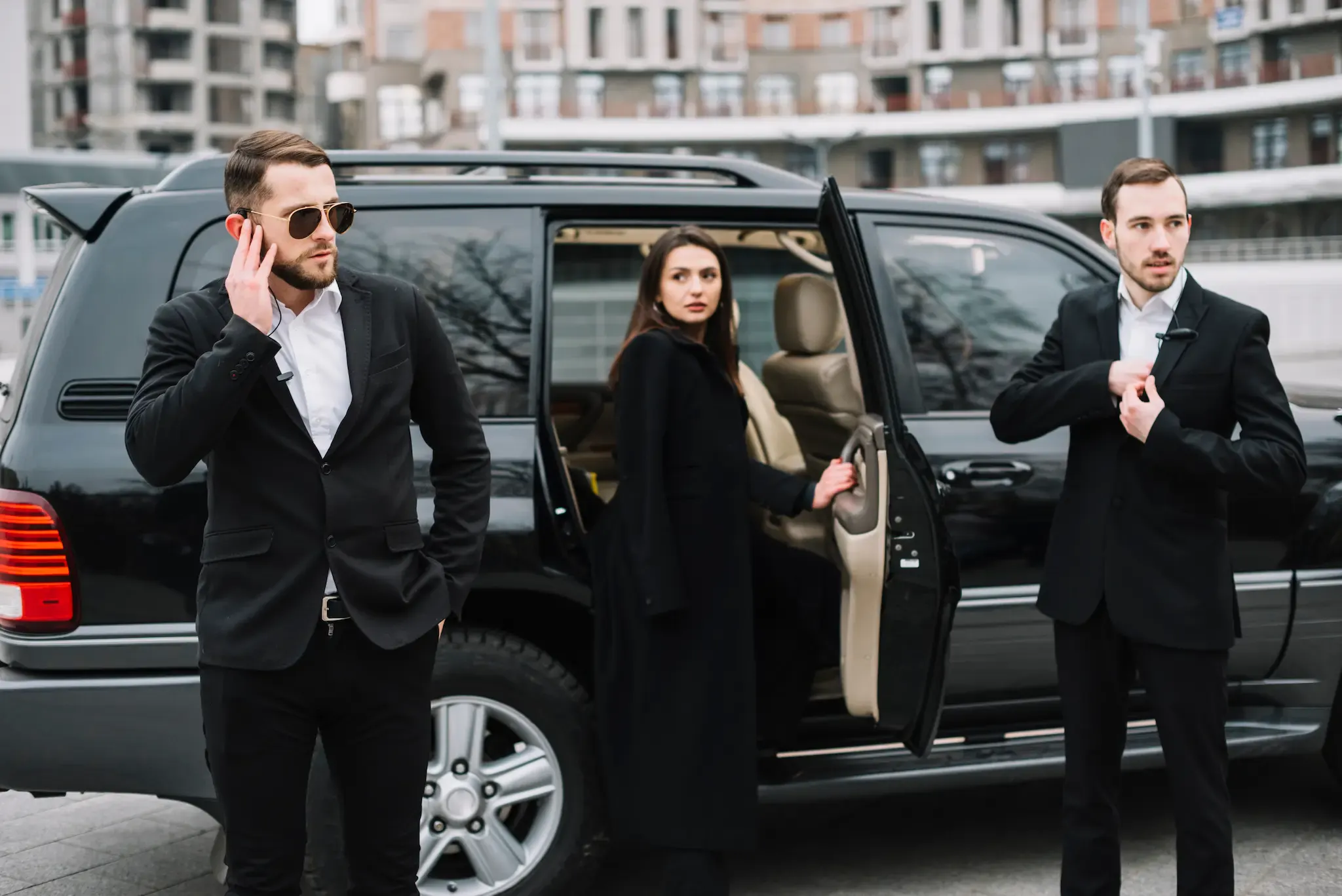 Two close protection officers standing watch as their client steps out of a black SUV