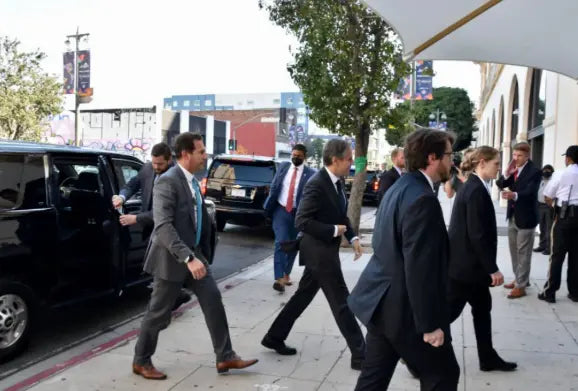 Security team in suits escorting a client along a city sidewalk near parked SUVs, indicating executive protection services.